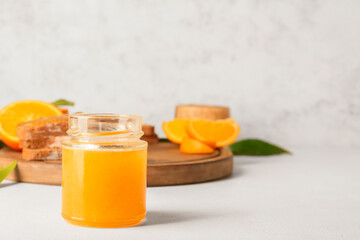 Glass jar of tasty orange jam on light background