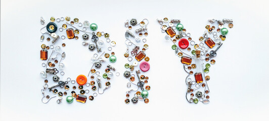 Diy lettering collected from handmade tools such as buttons, ear wires, locks, sequins, pendants on a white background. Craft and hobby concept