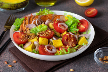 Salad with mango, smoked chicken and cherry tomatoes served with green lettuce leaves in a plate on a brown background