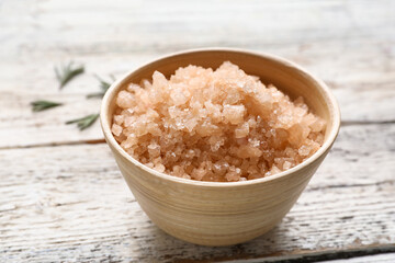 Bowl of sea salt on light wooden background, closeup
