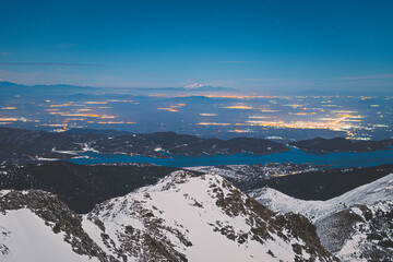 Moonlight snowy landscape with Plastiras lake and mount Kissavos on the background with the citylights from the nearby citys