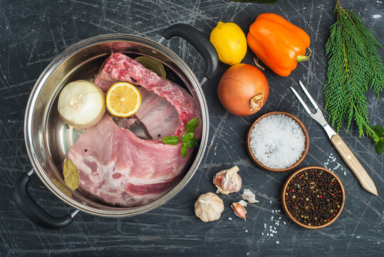 pot of water and meat prepared for boiling. seasonings and vegetables on a black table.