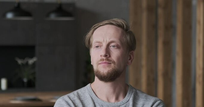 Portrait confident handsome European bearded man with green eyes focused face expression standing at loft kitchen. Stylish blonde male with trendy hairstyle having calmness emotion posing at apartment