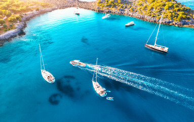 Aerial view of beautiful yachts and boats on the sea at sunset in summer. Akvaryum koyu in Turkey. Top view of luxury yachts, sailboats, clear blue water, rock, lagoon, coast, green trees. Travel