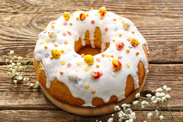Board with tasty Easter cake and gypsophila flowers on wooden background