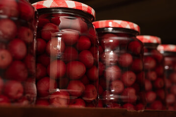 Close up of many cherry fruit compote in glass jars on a shelve. Preserved organic food, healthy homemade food concept - obrazy, fototapety, plakaty