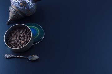 Coffee beans in a round jar, a teaspoon and a Turkish oil lamp on a black background