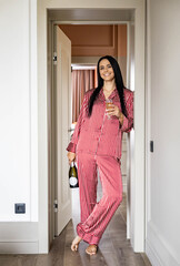 Cheerful domestic woman in red pajamas posing near door with champagne bottle and wine glass