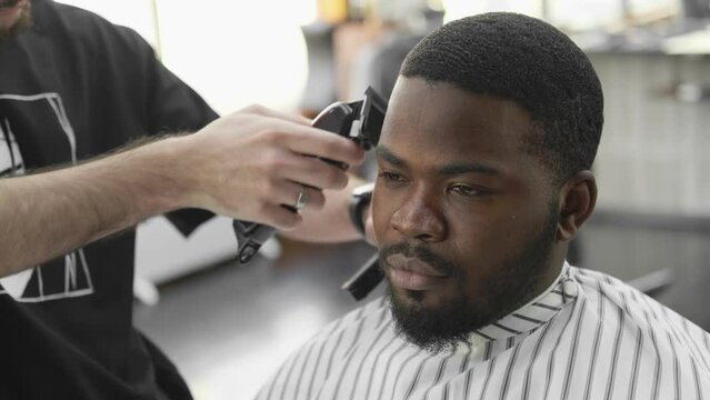 African American at the barbershop. Handsome black man getting his haircut in an African salon. Hairstyle. Looking straight ahead
