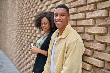 Fototapeta na wymiar Man and woman looking at camera standing near brick wall