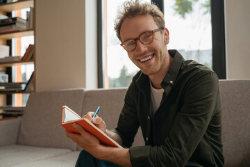 Portrait of young handsome man wearing stylish eyeglasses holding notebook, taking notes sitting at...