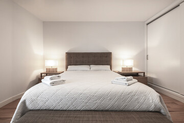Bedroom with king size bed, matching upholstered headboard and bench and clean white towels on the bedspread