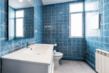 Bathroom with gloss white lacquered wooden cabinet with white resin basin, frameless rectangular mirror and walls tiled with kitsch blue tile