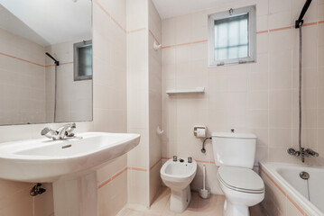 Conventional toilet with all white toilets, rectangular mirror and small window in the wall