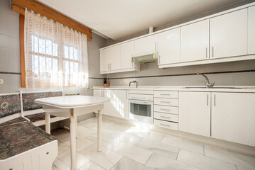 Kitchen with walls covered with white wood cabinets, white countertops and gray tiles, white marble floor and white wood corner table