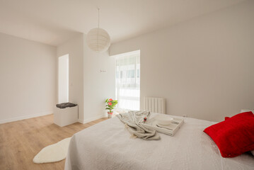 Bedroom with a king size bed with white walls and furniture, vegetal and red details on the cushions and oak wood floors