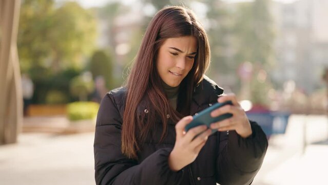 Young hispanic woman smiling confident playing video game at street