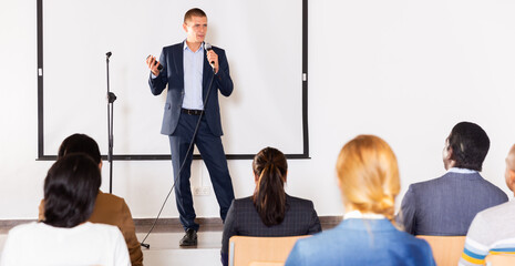 Successful business coach speaking from stage to audience at corporate training