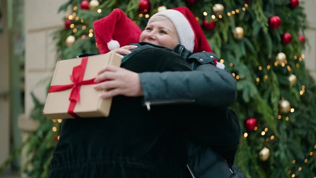 Mother and son wearing christmas hat surprise with gift at park