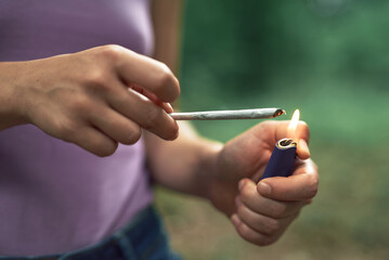 Young woman's hands lighting a piece of marihuana in rolling cigarette paper, ready to make a joint