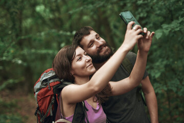 Two friends, hikers, taking a selfie in the forest, updating social media from their adventurous woods exploration