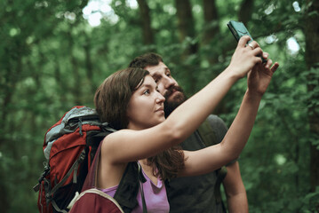 Two friends, hikers, taking a selfie in the forest, updating social media from their adventurous...