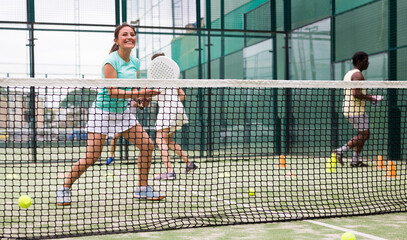 Portrait of cheerful woman paddle tennis player performing strokes technique at group training at court