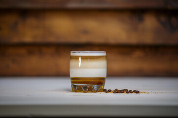 Layered coffee with cinamon in short glass on table with wood background and coffee beans