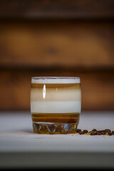 Layered coffee with cinamon in short glass on table with wood background and coffee beans