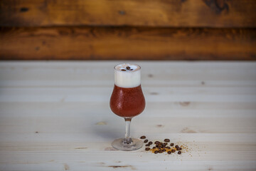 Crushed ice coffee with cinamon in brandy glass from angle on table with wood background and coffee beans