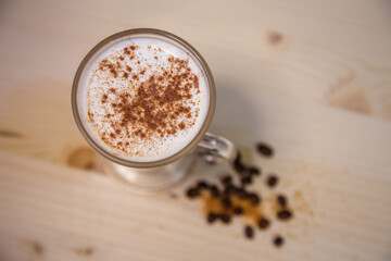 Cappucino with cinamon in tall glass from above on table with wood background and coffee beans