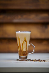 Cappucino with cinamon in tall glass on table with wood background and coffee beans