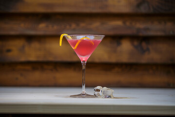 Fresh cosmopolitan martini with lemon twist on table with wood background