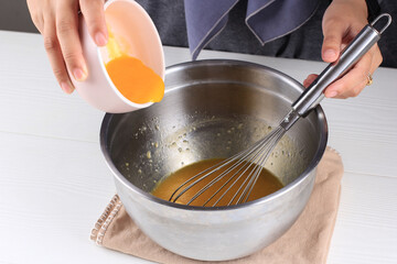 Female hands pour melted butter from a white bowl into crumbled biscuits while making a homemade dessert.