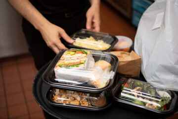 A view of an employee attending to a tray full of to-go containers, in a restaurant kitchen setting.