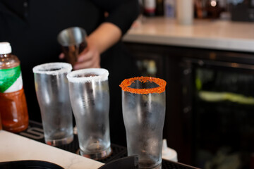A view of a bartender preparing chili lime salt garnished cocktails at the bar.