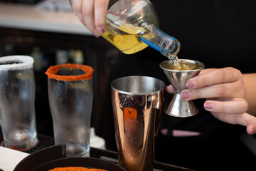 A view of a bartender using a jigger to measure a shot of liquor for some prepared cocktails at the bar counter.