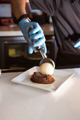 A view of a restaurant employee preparing a plate of brownie a la mode.