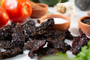 A closeup view of a pile of chile morita, among other salsa ingredients.