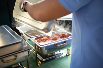A view of a person lifting the lid of a chafer dish, seeing warm steaming food inside.