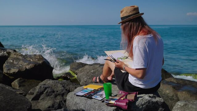 Woman artist painting sea and rocks from life