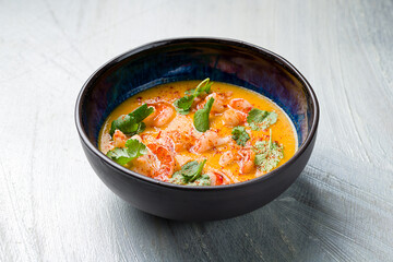 Tom Yam soup with shrimps on blue bowl on grey table