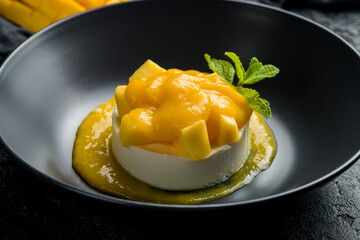panna cotta with mango and mint on black bowl on dark stone table, Chinese cuisine macro close up