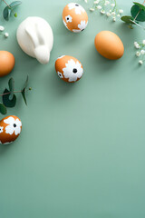 Happy easter concept. Easter painted eggs, bunny, eucalyptus and gypsophila on green table. Top view, flat lay. Minimal style.