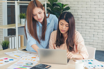 Happiness two women working together confident team meeting in office desk. Team business partners working with computer laptop startup company. Asian colleague friendship at work with smiling face.