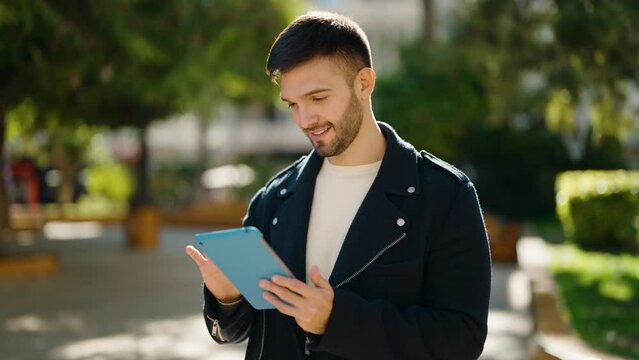 Young hispanic man smiling confident using touchpad at park