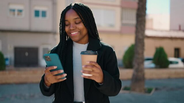 Young african american woman using smartphone drinking coffee at street