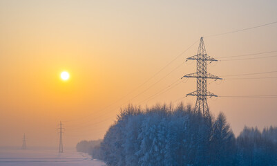 winter morning landscape of snow covered nature, trees and large poles of high voltage power transmission lines