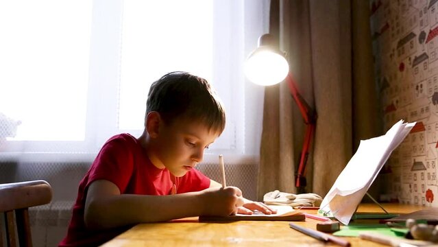 Portrait of concentraited Caucasian child doing homework at the table at home. Thoughtful schoolboy. Education, studying, learning