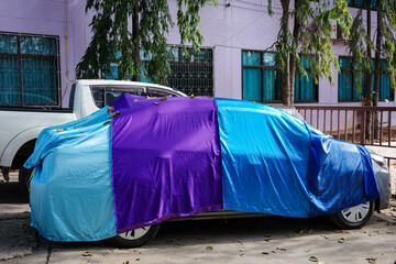 Sedan car at outdoor parking area covered by blue and purple fabric car cover.